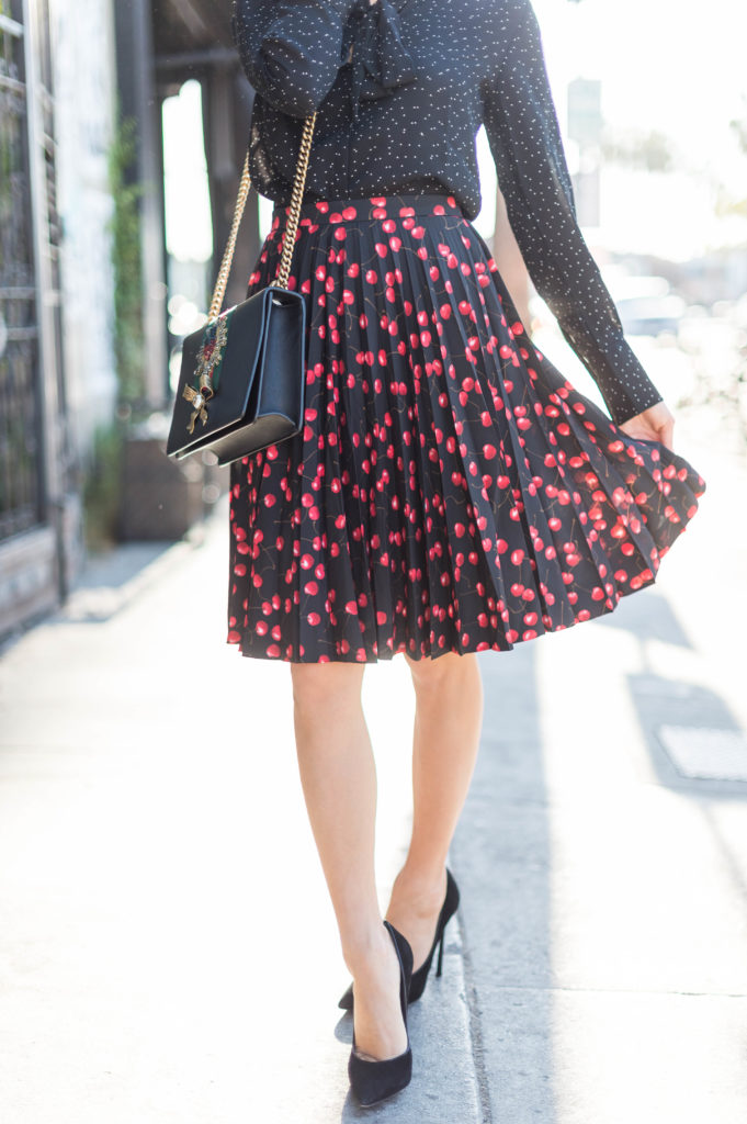 Lifestyle and corporate blogger Amanda Warsavsky wearing a J. Crew cherry skirt and a Banana Republic black bow blouse and Gucci bag