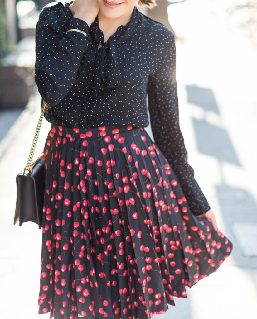 Lifestyle and corporate blogger Amanda Warsavsky wearing a J. Crew cherry skirt and a Banana Republic black bow blouse and Gucci bag