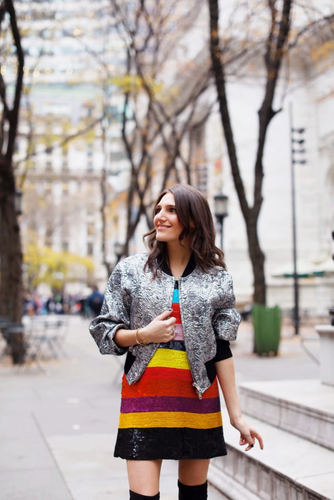 That Pencil Skirt, a fashion blogger, wearing an Alice and Olivia striped sequin color mini dress, with a Philip Lim silver embroidered bomber jacket and over the knee black suede boots